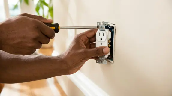 Close-up of hands screwing a new white wall outlet into place